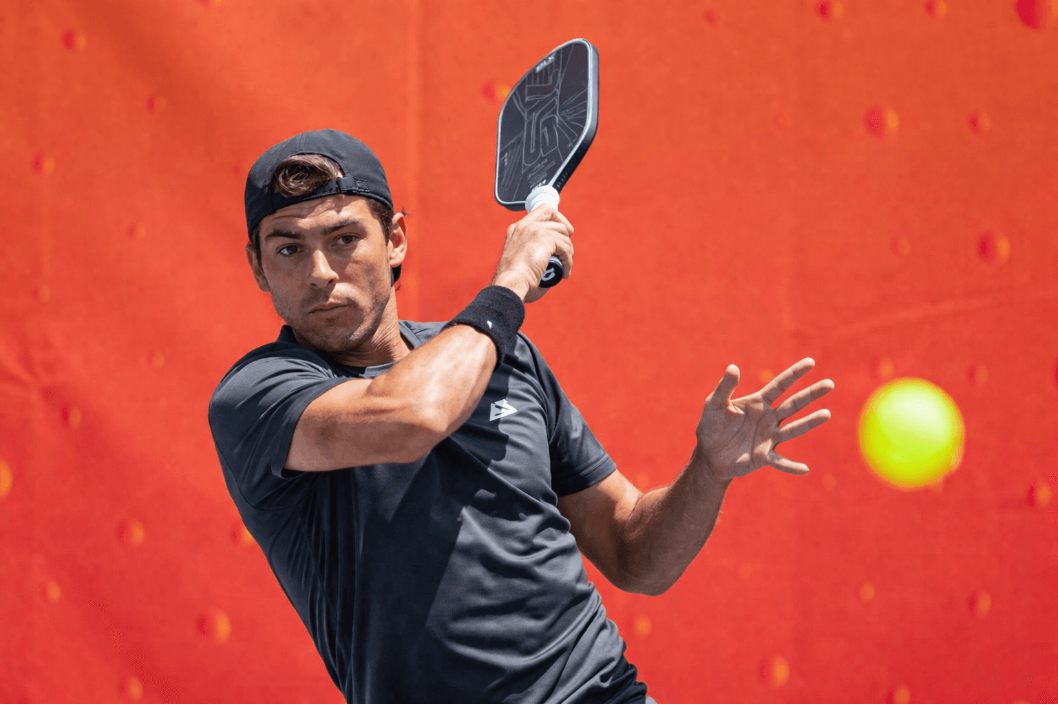 A pickleball player preparing to strike against a bold orange court backdrop